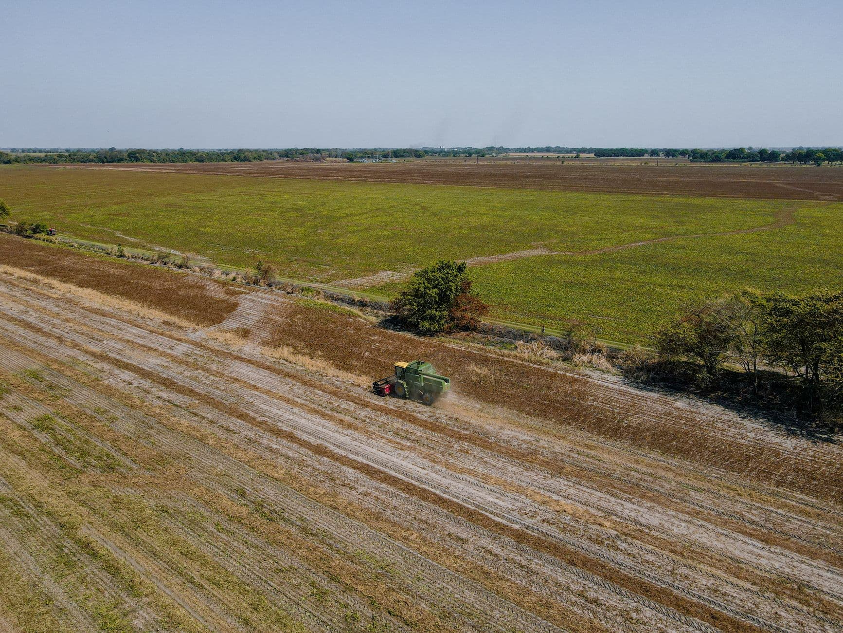 Aerial shot of a combine harvester working in a large, open field under clear skies.