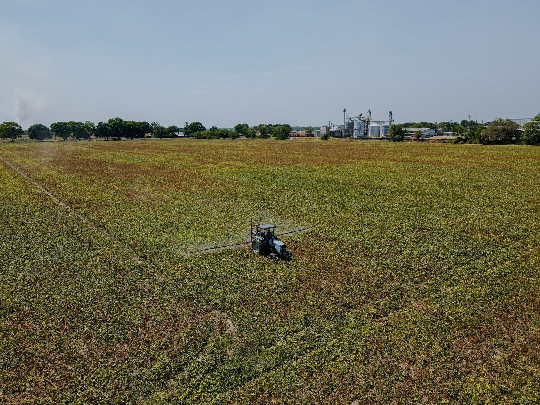 Aerial shot of a tractor spraying crops in an expansive agricultural field during the day.