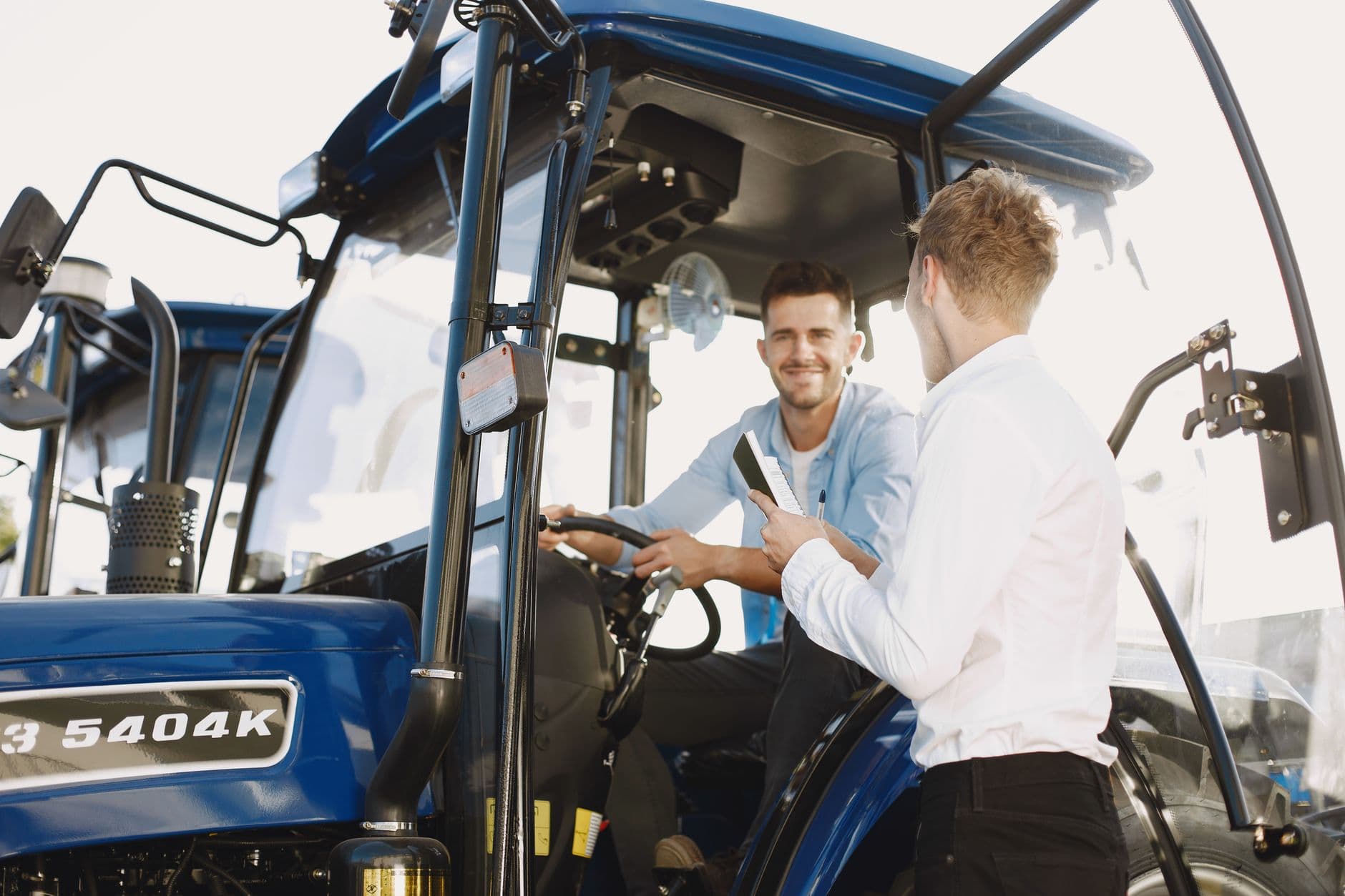 Two men engaged in a discussion about a tractor sale, set in an outdoor environment.